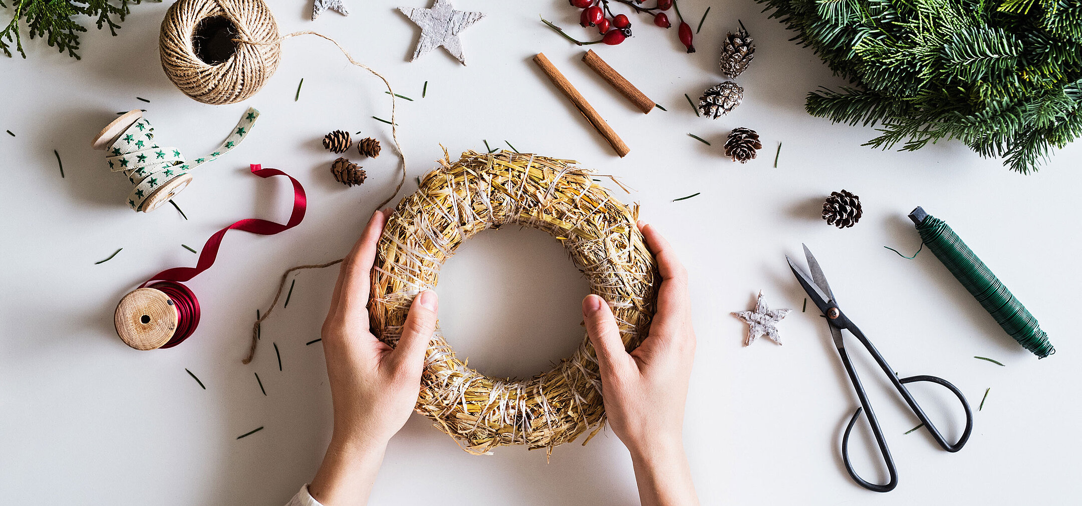 © Halfpoint - AdobeStock.com Hands arranging an Advent wreath on a table with fir branches, ribbons and craft materials.