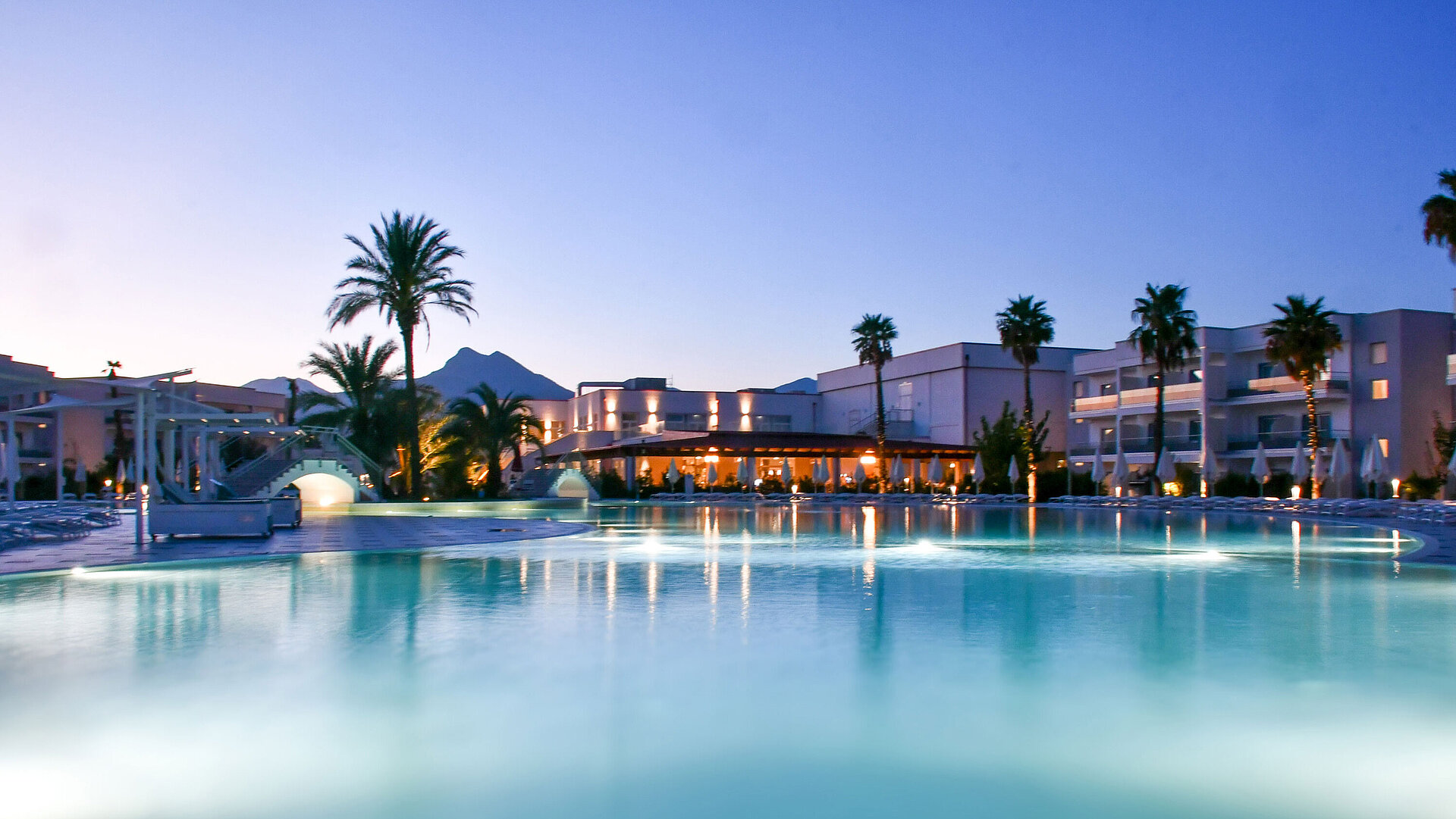 Luci serali alla piscina del Maritim Resort Calabria con palme e montagna