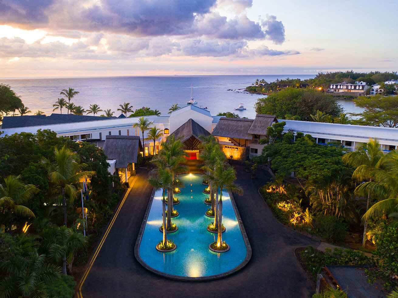 Entrance of the hotel Hotel complex with illuminated pool and palm trees at sunset by the sea