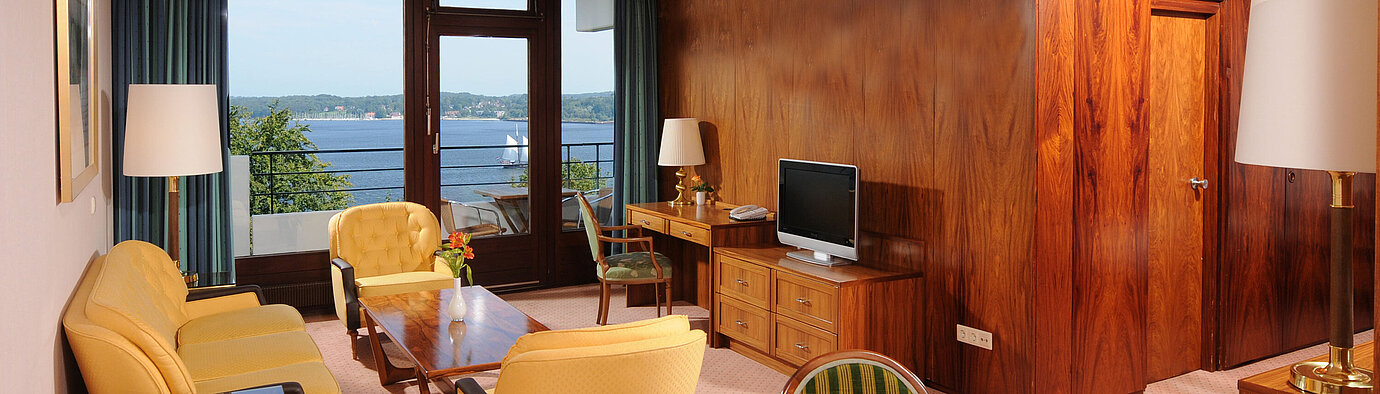 Suite Junior Junior Suite en el Maritim Hotel Kiel, acogedora zona de estar, escritorio, TV y balcón con vistas al agua.