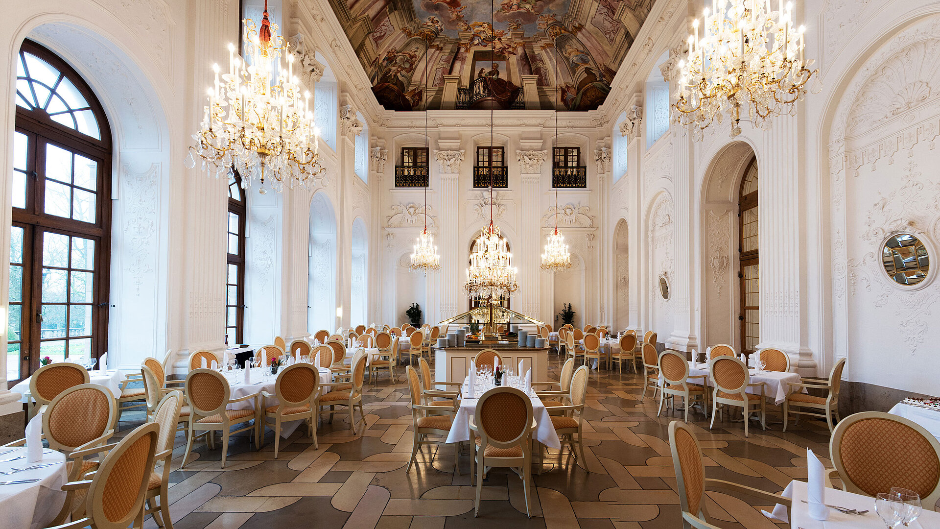 Elegant Apollo Hall at Maritim Hotel Fulda with chandeliers, fresco ceiling, and stylishly set tables.