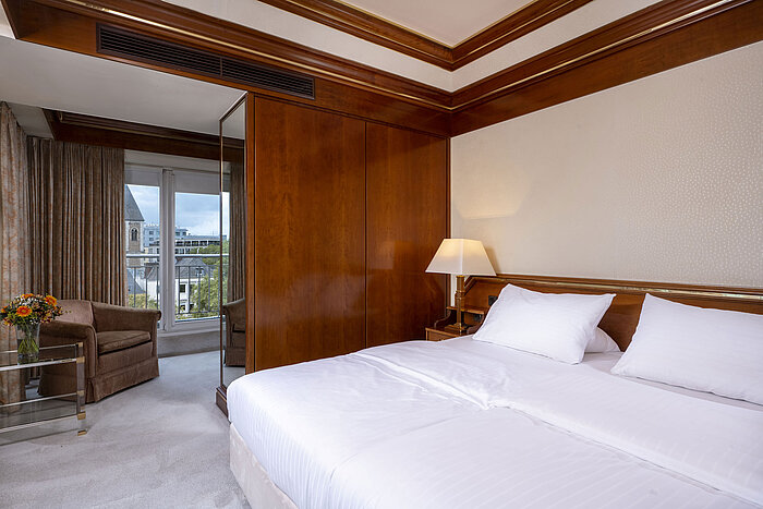 Camera luminosa nella suite Heumarkt del Maritim Hotel Colonia con letto matrimoniale, dettagli in legno e accesso al balcone