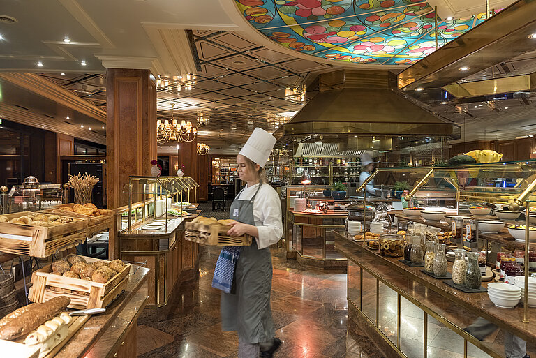 Buffet della colazione presso Maritim Hotel Bremen con panini freschi, pane e una selezione di piatti, servito da una chef.