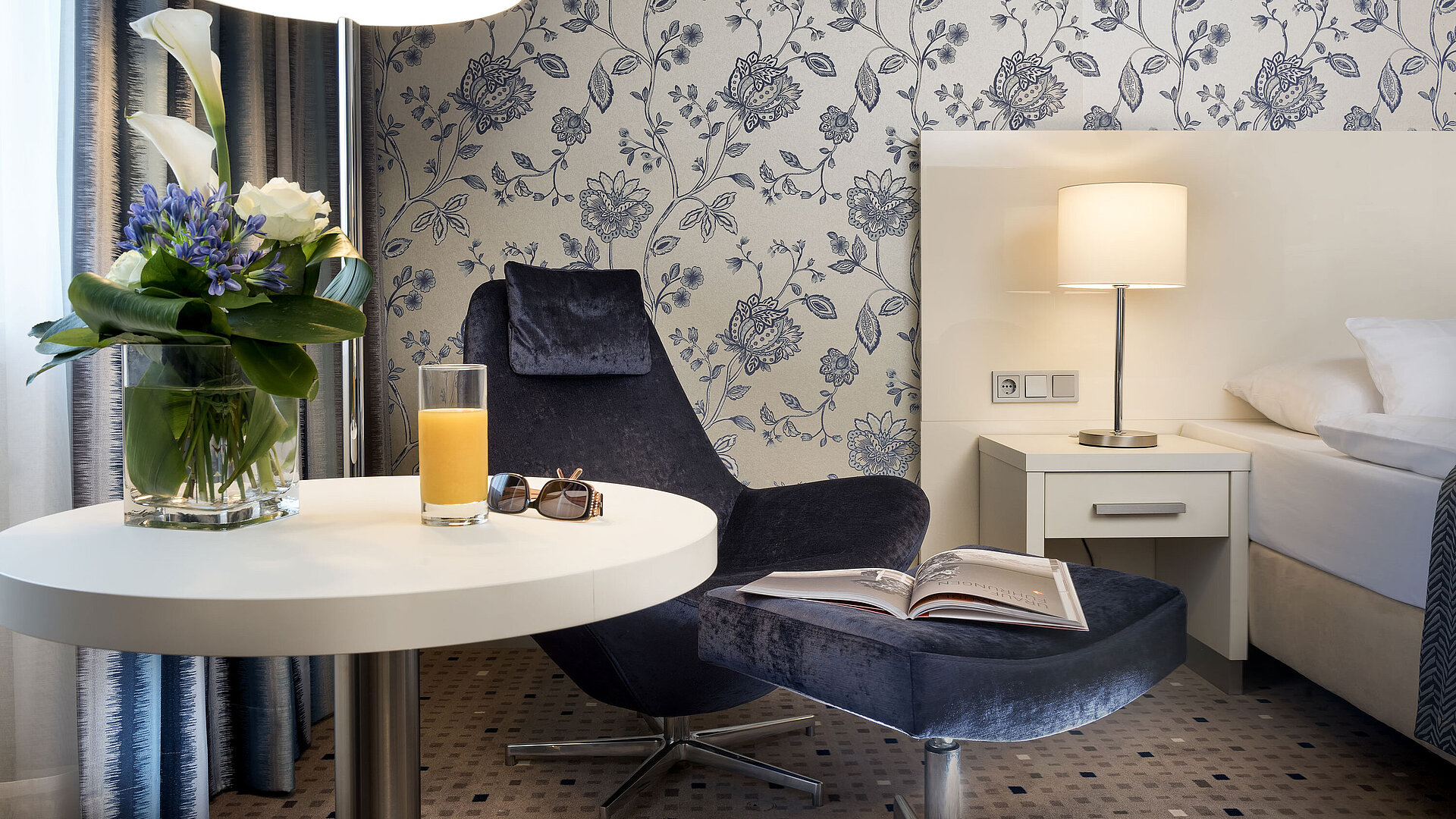 Superior room at Maritim Hotel Bonn with stylish decor, cozy armchair, floral arrangement, and modern lighting.