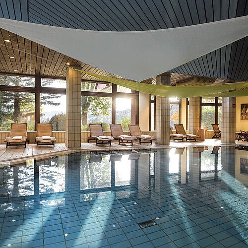 Piscine intérieure lumineuse avec transats et vue sur le jardin à l’hôtel Maritim Titisee
