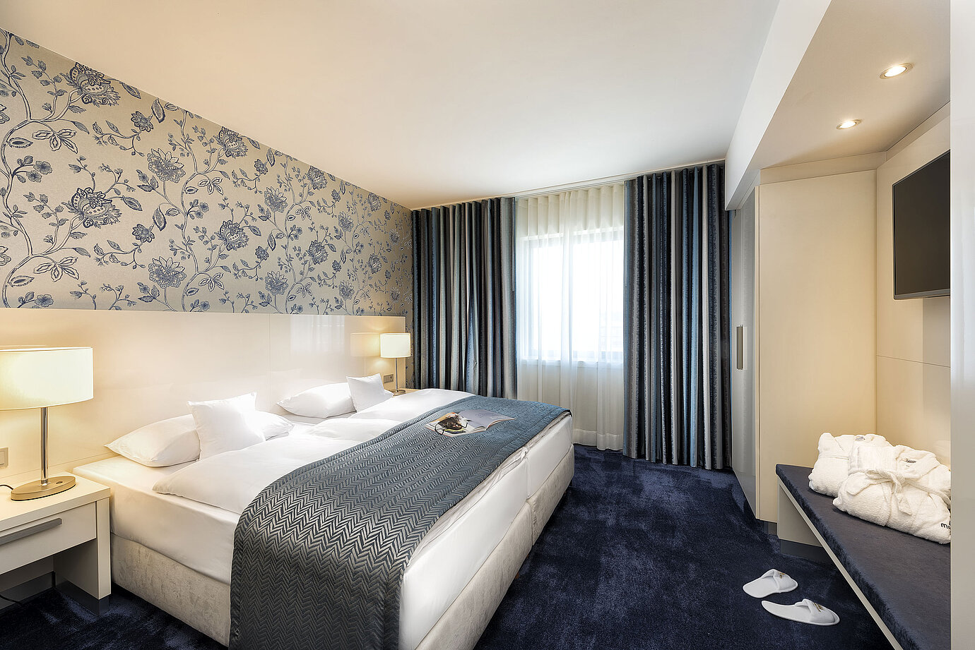 Suite elegante presso il Maritim Hotel Bonn con un grande letto, copriletto blu e arredi eleganti.