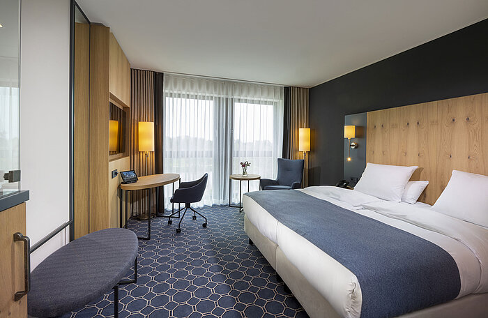 Habitación doble espaciosa en el Maritim Hotel Ingolstadt con escritorio, zona de estar y balcón.