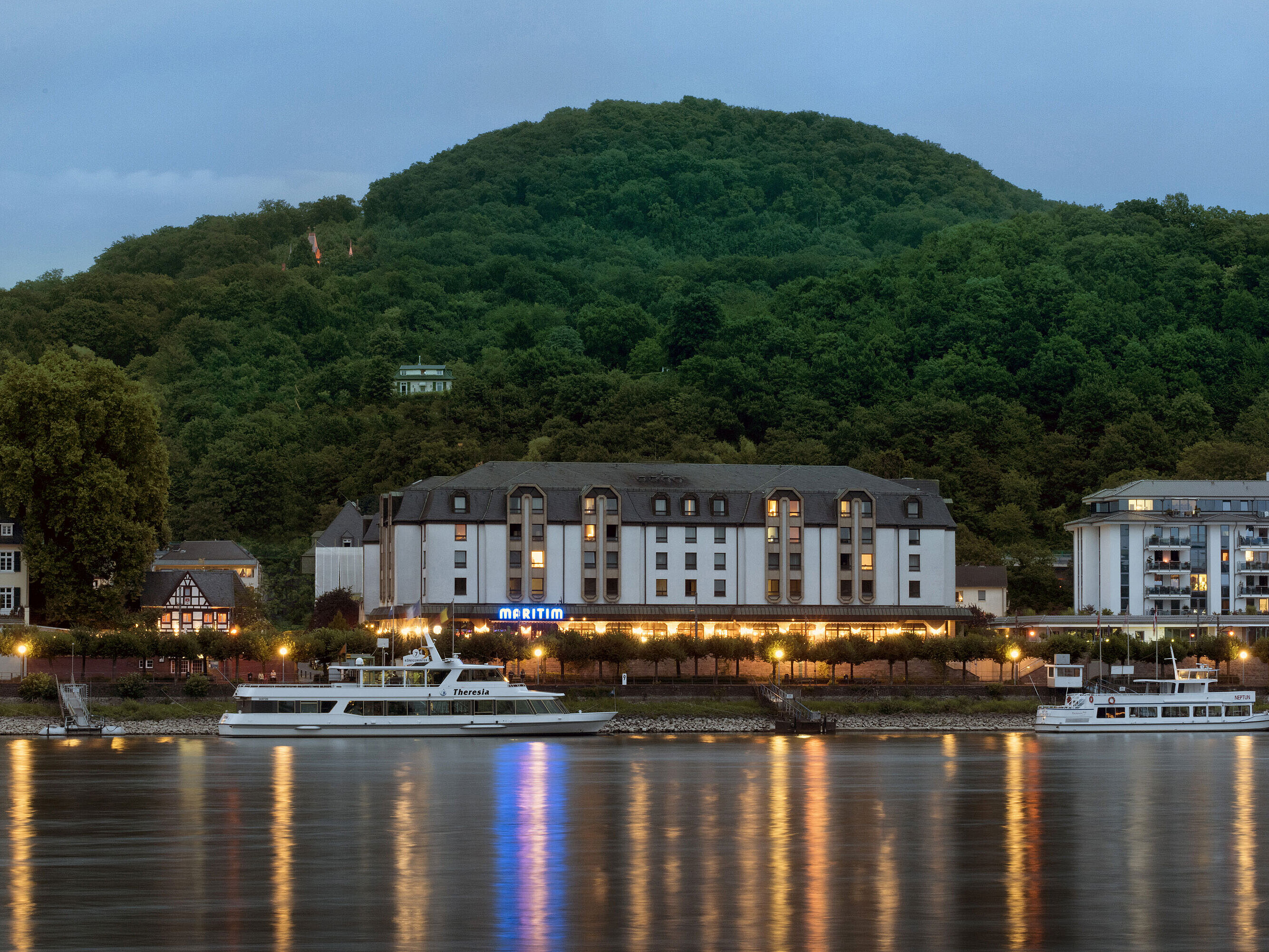 Hôtel Maritim Königswinter de nuit avec éclairage chaleureux et vue sur le Rhin.