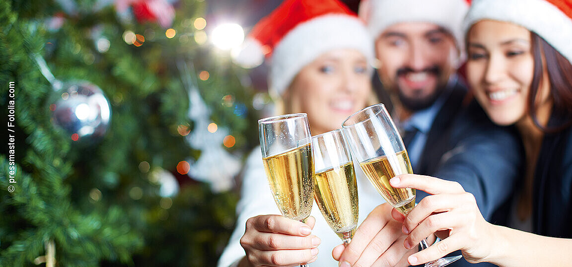 © pressmaster - fotolia Friends in Christmas hats clinking champagne glasses in front of a decorated Christmas tree