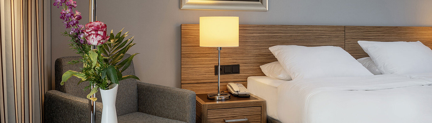 Accogliente angolo salotto con vaso di fiori accanto al comodo letto nella camera Superior del Maritim Hotel Darmstadt