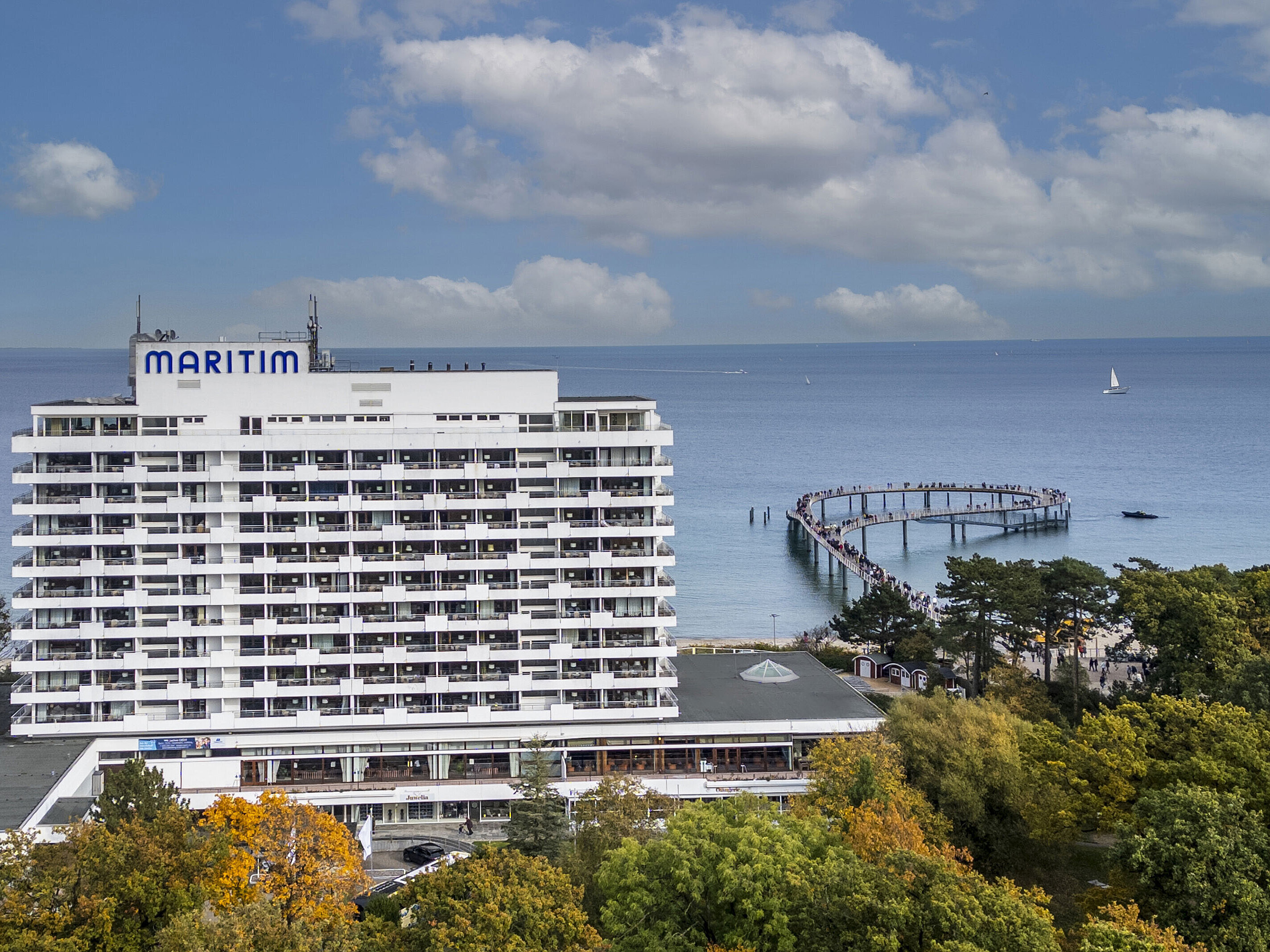 Maritim Seehotel Timmendorfer Strand con vista sul pontile e sul Mar Baltico, circondato da alberi e cielo azzurro.