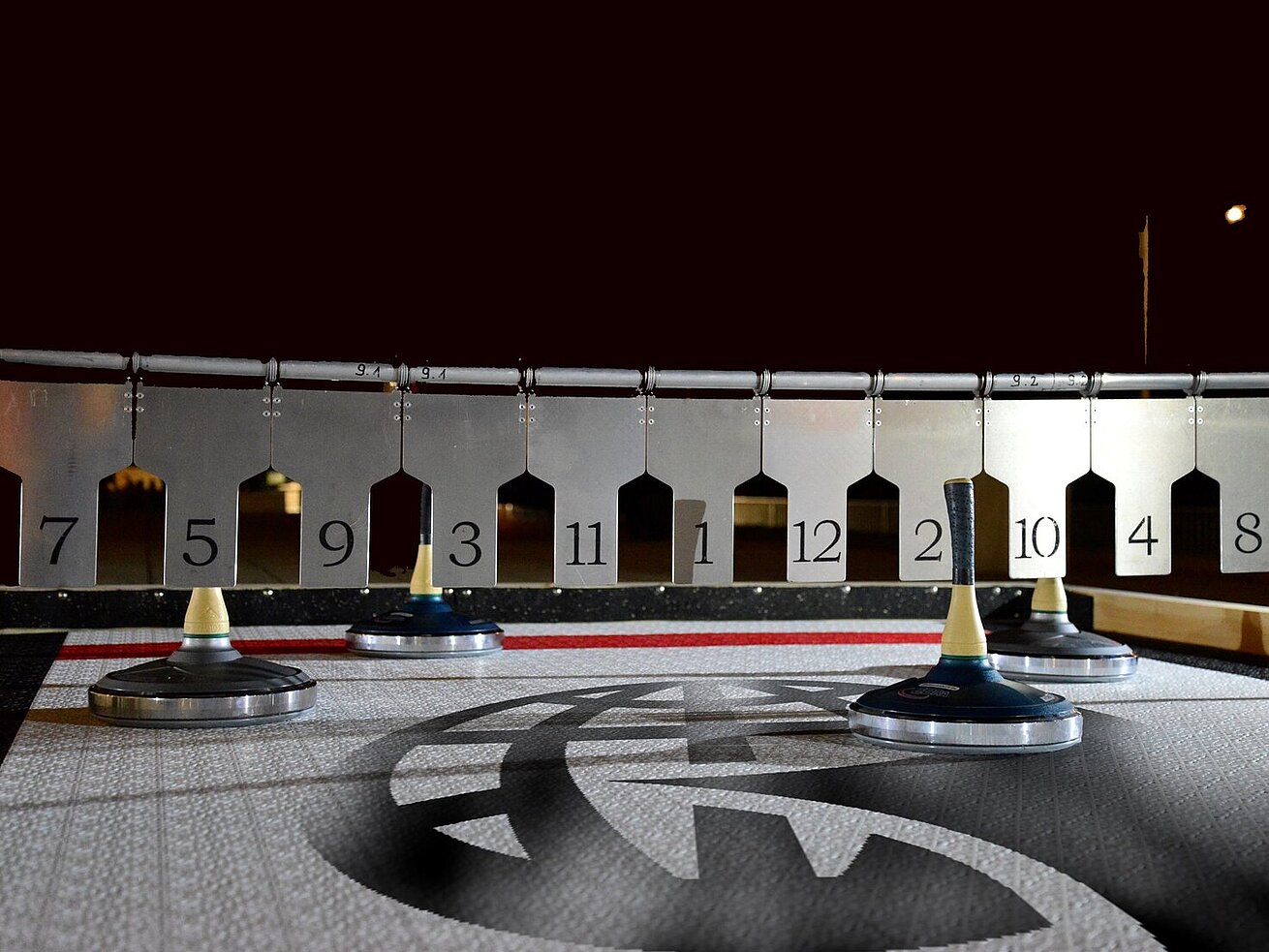 Guests playing Bavarian curling on a lit outdoor rink at night with marked target circles.