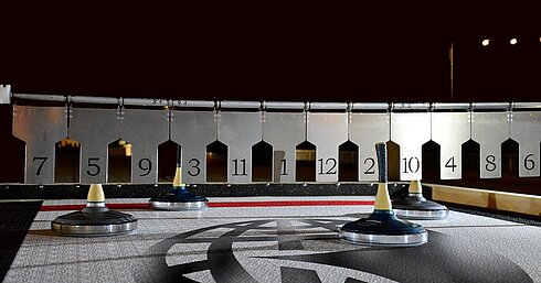 Guests playing Bavarian curling on a lit outdoor rink at night with marked target circles.