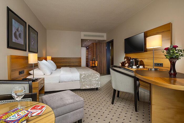 "Chambre confort à l'hôtel Maritim Bad Homburg avec lit double, cartes à jouer, ours en peluche et décor en bois élégant.