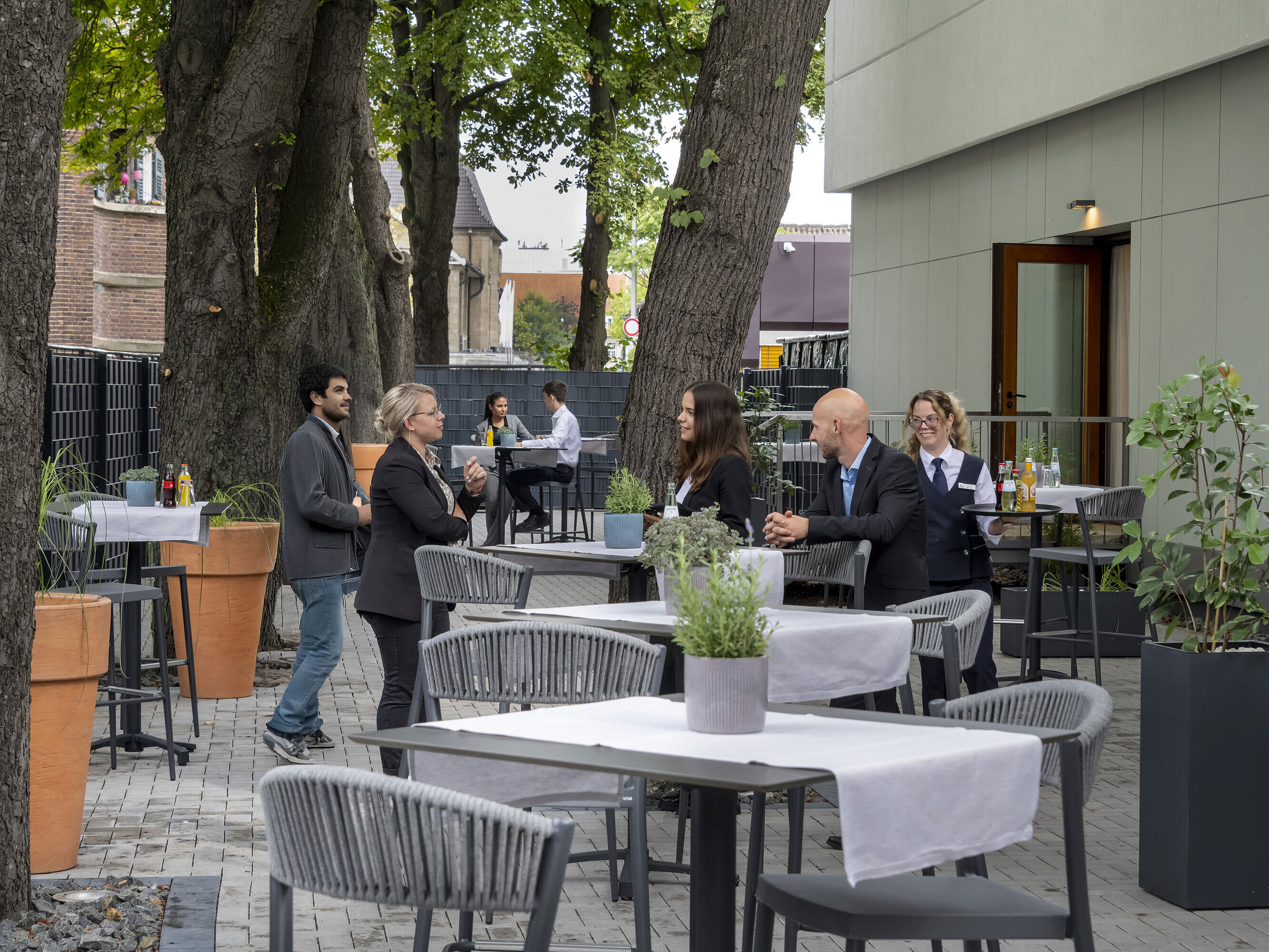 Modern terrace at Maritim Hotel Darmstadt with guests relaxing, trees in the background, and stylish gray furniture.