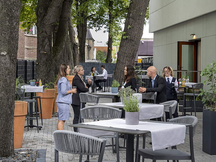 Modern terrace at Maritim Hotel Darmstadt with guests relaxing, trees in the background, and stylish gray furniture.