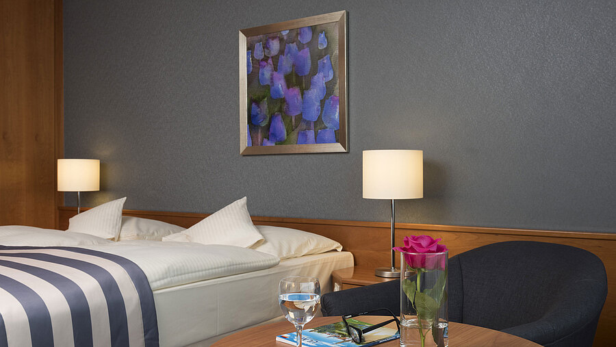 Detalle en el Maritim Hotel Ulm: rosa, agua, gafas y folleto sobre la mesa junto a la cama