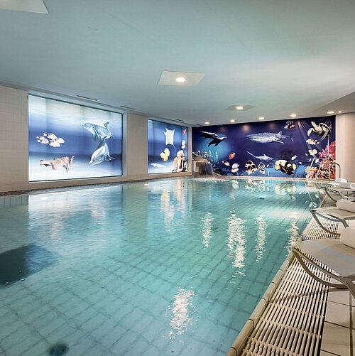 Piscine intérieure de l'hôtel Maritim avec des chaises longues et une décoration impressionnante sous-marine sur les murs.