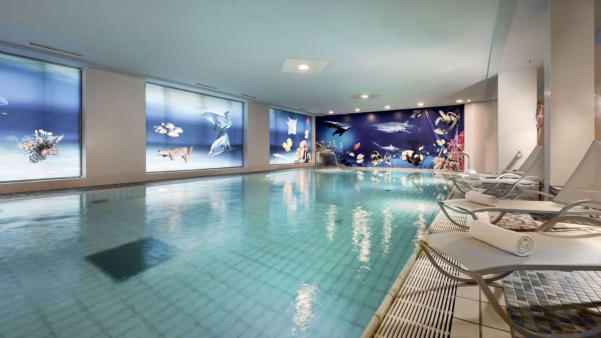 Piscine intérieure de l'hôtel Maritim avec des chaises longues et une décoration impressionnante sous-marine sur les murs.