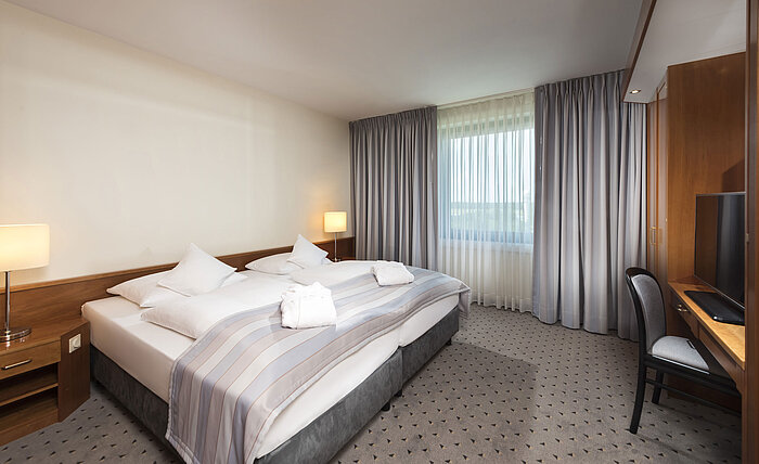 Junior Suite con letto matrimoniale, TV, scrivania e ampie finestre al Maritim Hotel Hannover.
