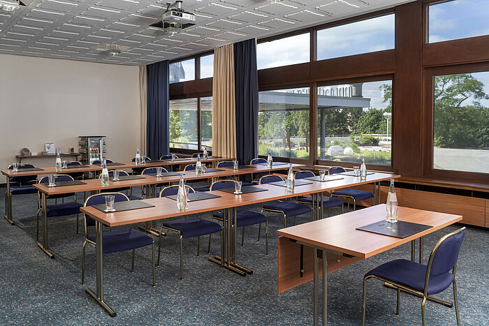 Sala con filas de sillas, moqueta y grandes ventanales en el Maritim Hotel Travemünde