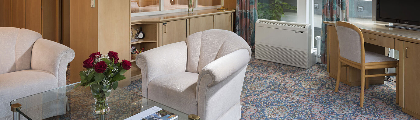 Salon élégant avec fauteuils, TV, grandes fenêtres et vue sur le toit au Maritim Hotel Bad Wildungen