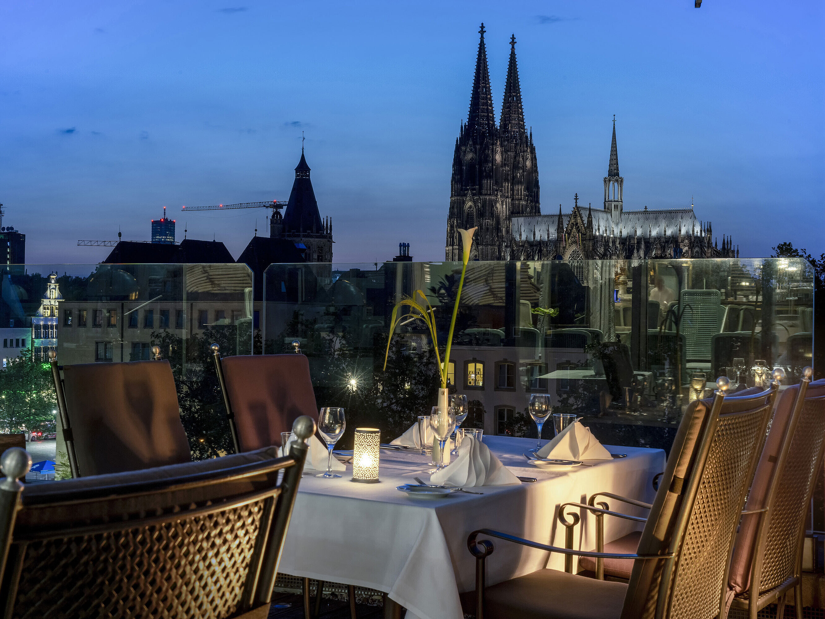 Set table on the illuminated rooftop terrace of Maritim Hotel Cologne at night with a view of Cologne Cathedral.