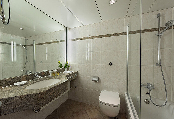 Baño luminoso con lavabo de granito, espejo y ducha – Maritim Hotel Travemünde