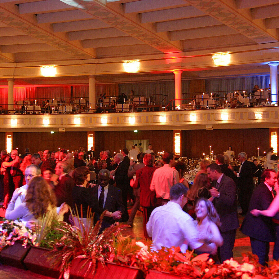 Event in the large hall of the Maritim Hotel Bonn with dancing guests, illuminated hall and filled galleries.