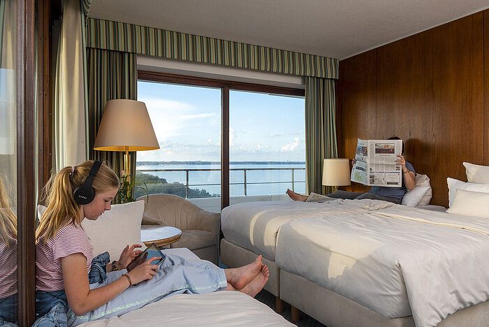 Chambre familiale avec vue sur le parc à l'hôtel Maritim Timmendorfer Strand, un enfant avec tablette et une personne avec un journal.