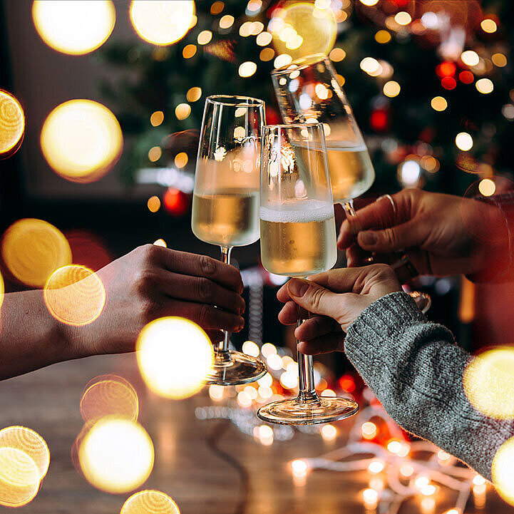 Three people clinking champagne glasses in front of a festively lit Christmas tree