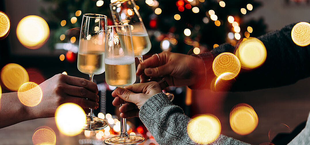 © Gregory Lee - AdobeStock.com Three people clinking champagne glasses in front of a festively lit Christmas tree