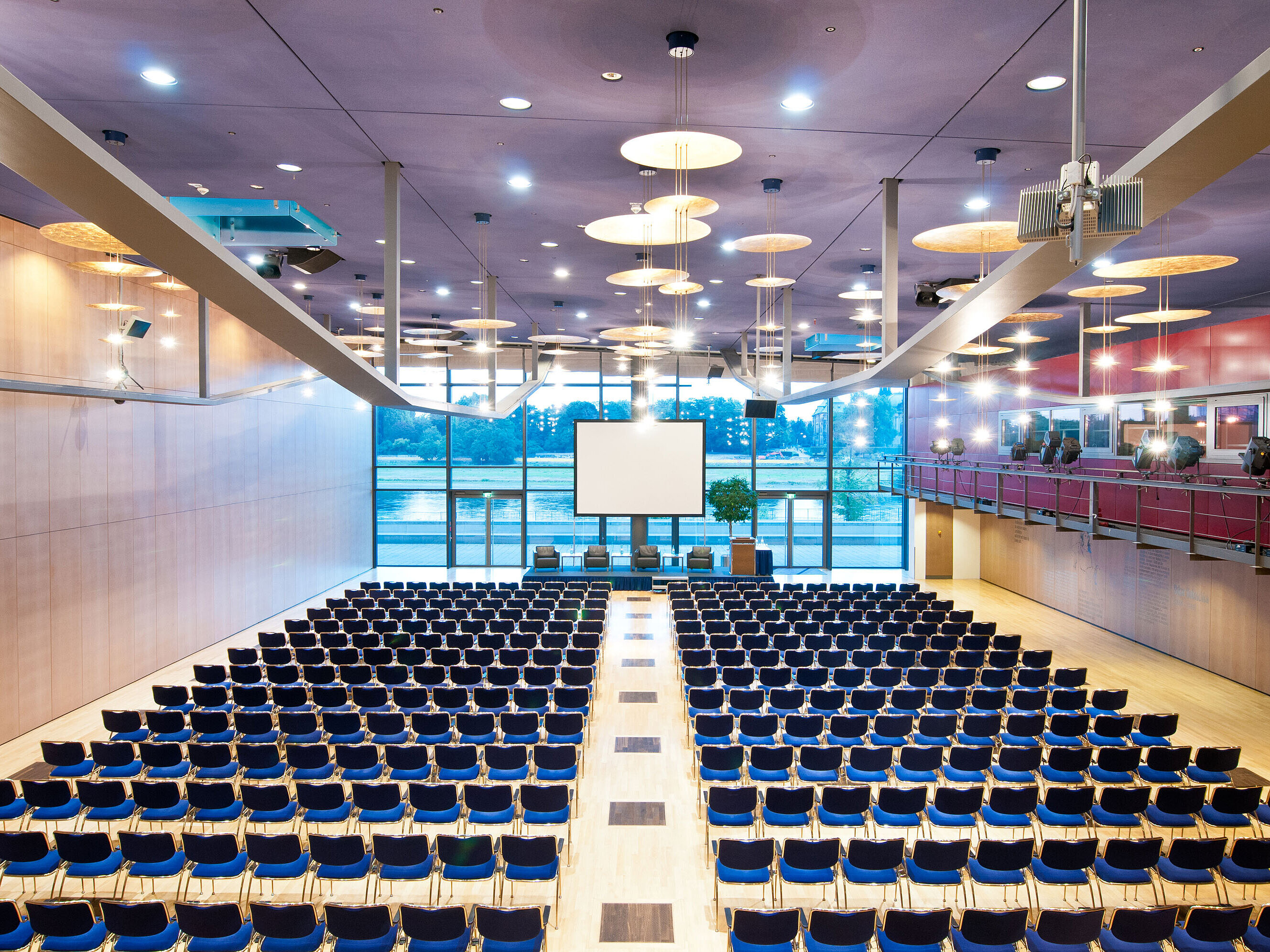 Gran sala de conferencias del Maritim Hotel Dresde con filas de sillas azules y vista al río Elba.