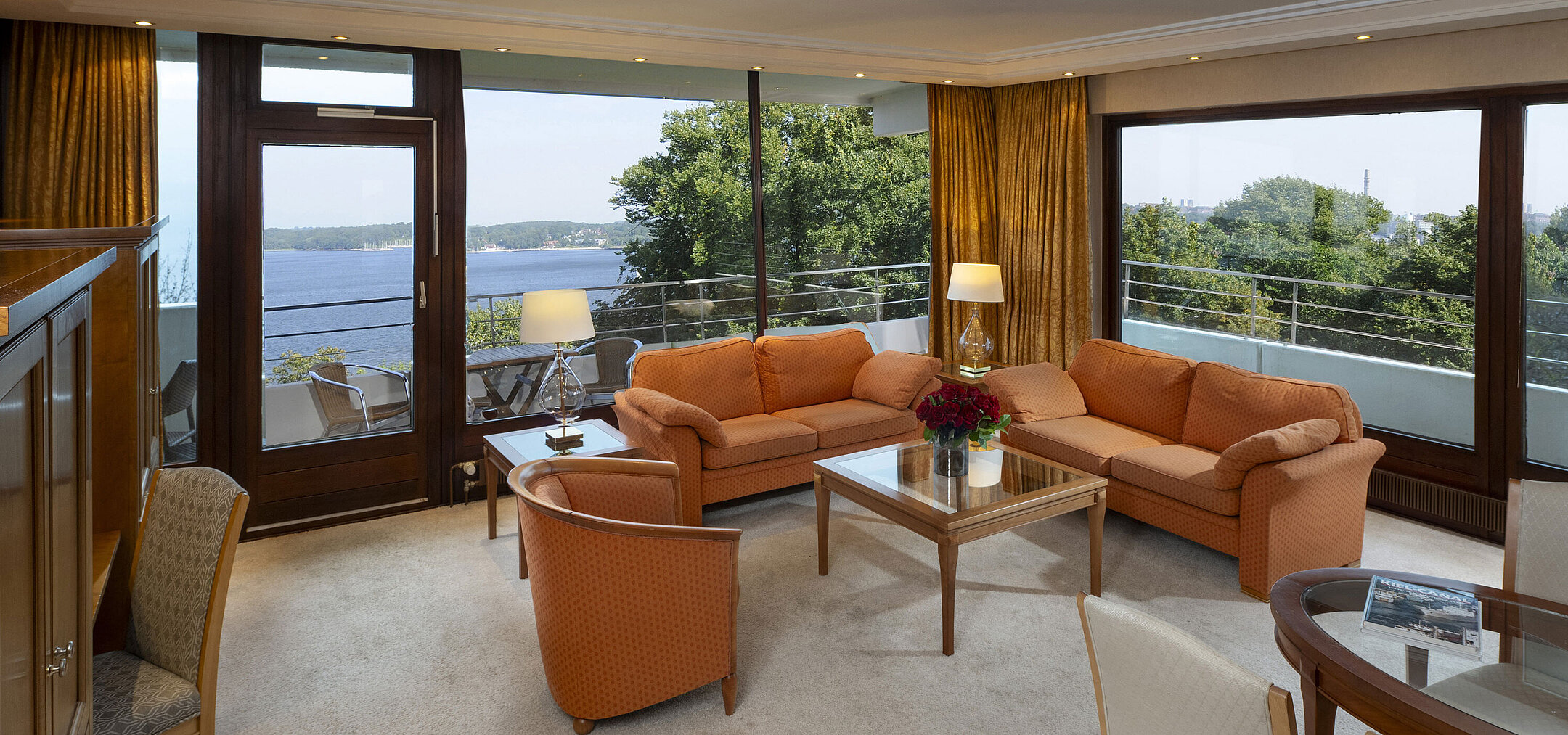 Luminoso soggiorno della suite presidenziale al Maritim Hotel Kiel con vista panoramica sul Mar Baltico e arredi eleganti.