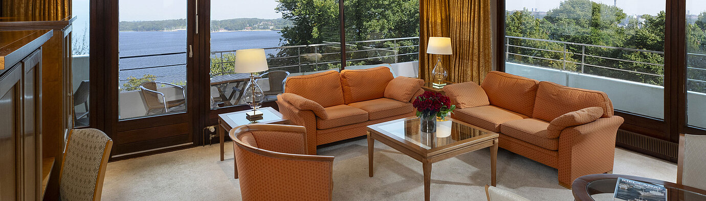 Sala de estar luminosa de la suite presidencial en el Maritim Kiel con vista panorámica al mar Báltico y muebles elegantes.