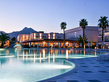 Evening lights at the pool of Maritim Resort Calabria with palm trees and mountain backdrop