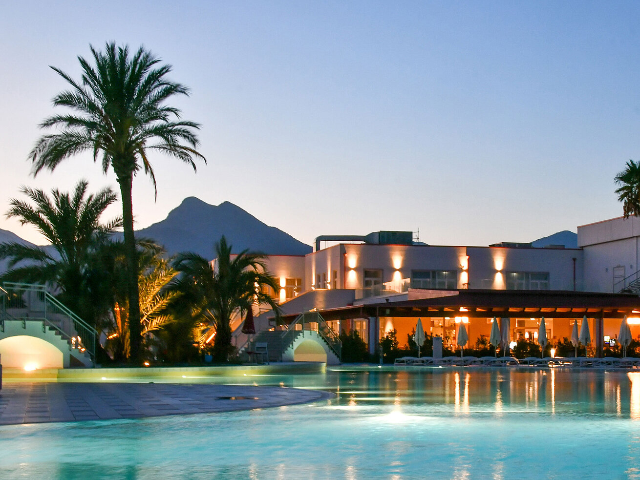 Evening lights at the pool of Maritim Resort Calabria with palm trees and mountain backdrop
