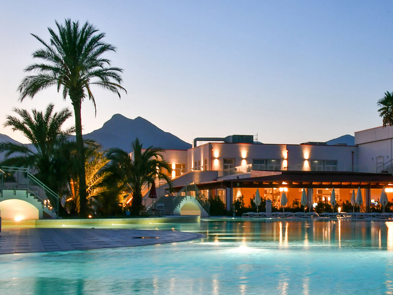 Pool Evening lights at the pool of Maritim Resort Calabria with palm trees and mountain backdrop