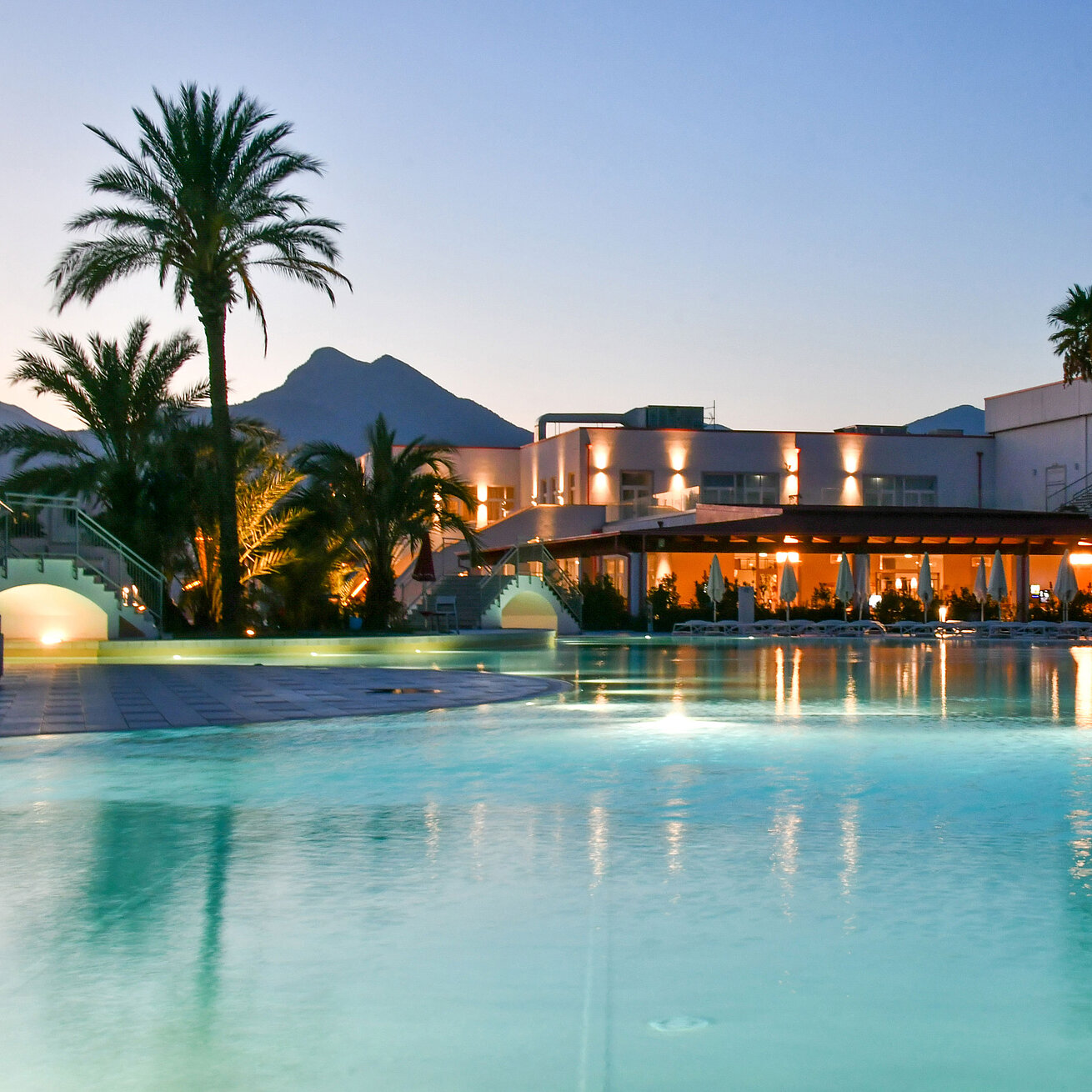Evening lights at the pool of Maritim Resort Calabria with palm trees and mountain backdrop