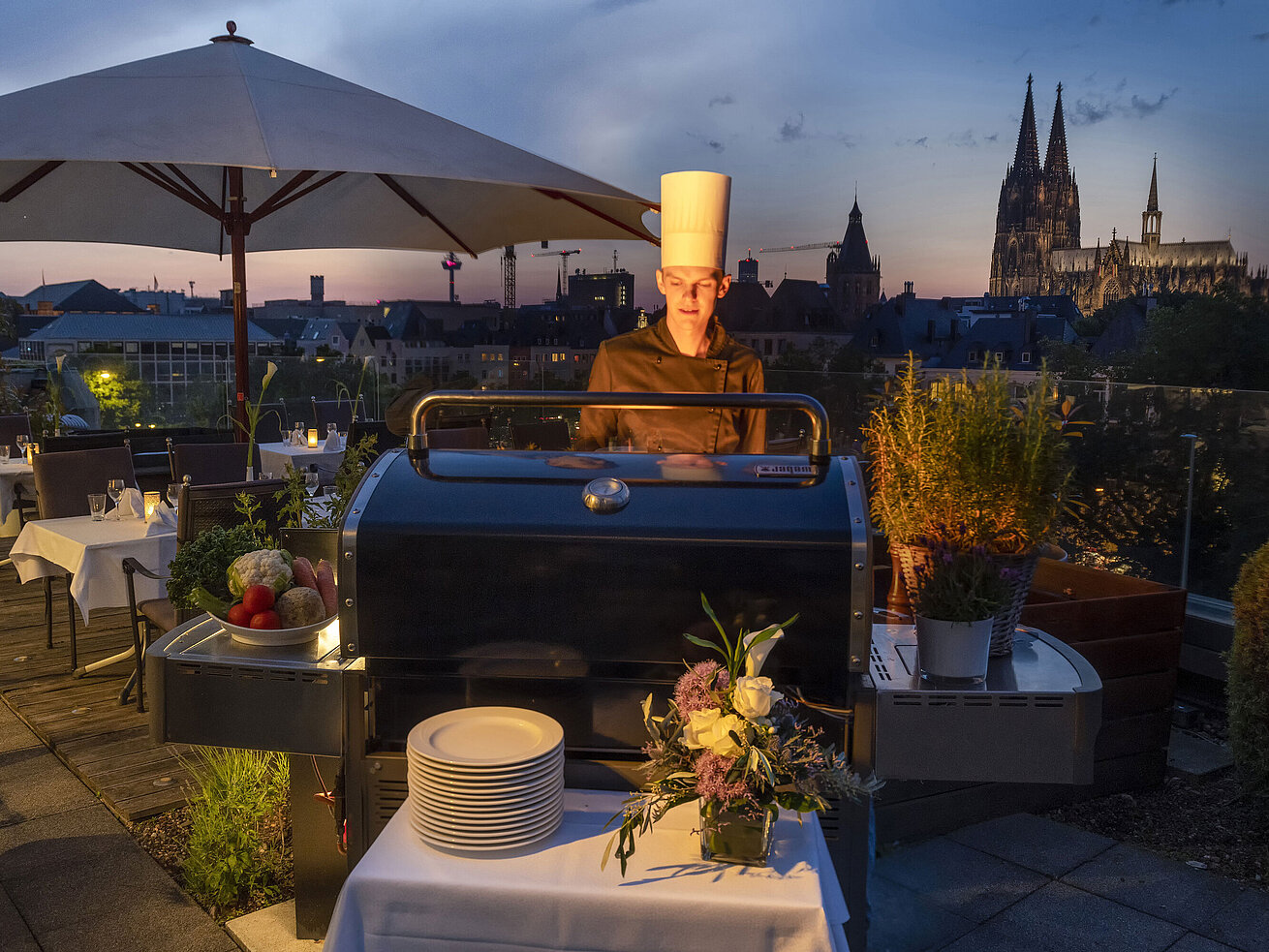 Rooftop terrace A chef grilling in the evening on the rooftop terrace with the illuminated Cologne Cathedral in the background.
