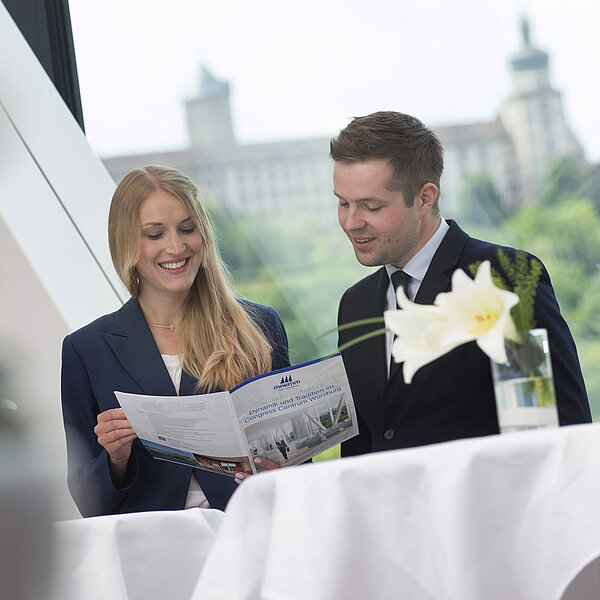 Due persone parlano al Maritim Hotel Würzburg con opuscolo e vista sulla fortezza