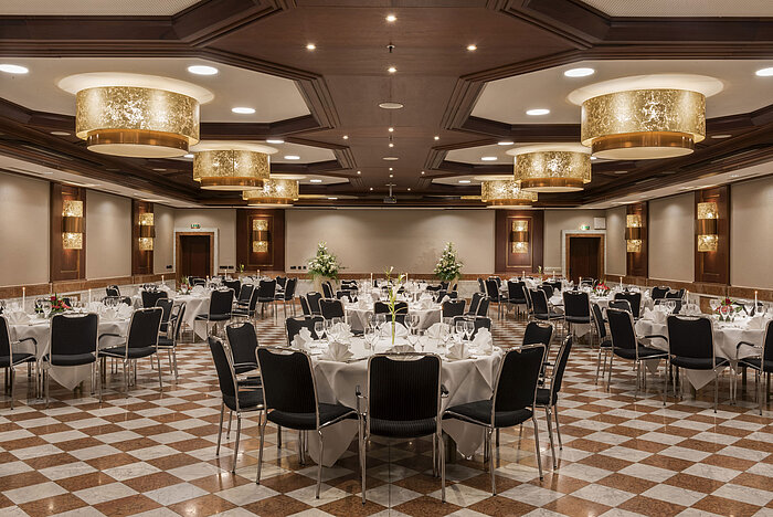 Elegante salón de eventos en Maritim Hotel Königswinter con mesas redondas, decoración elegante y lámparas.