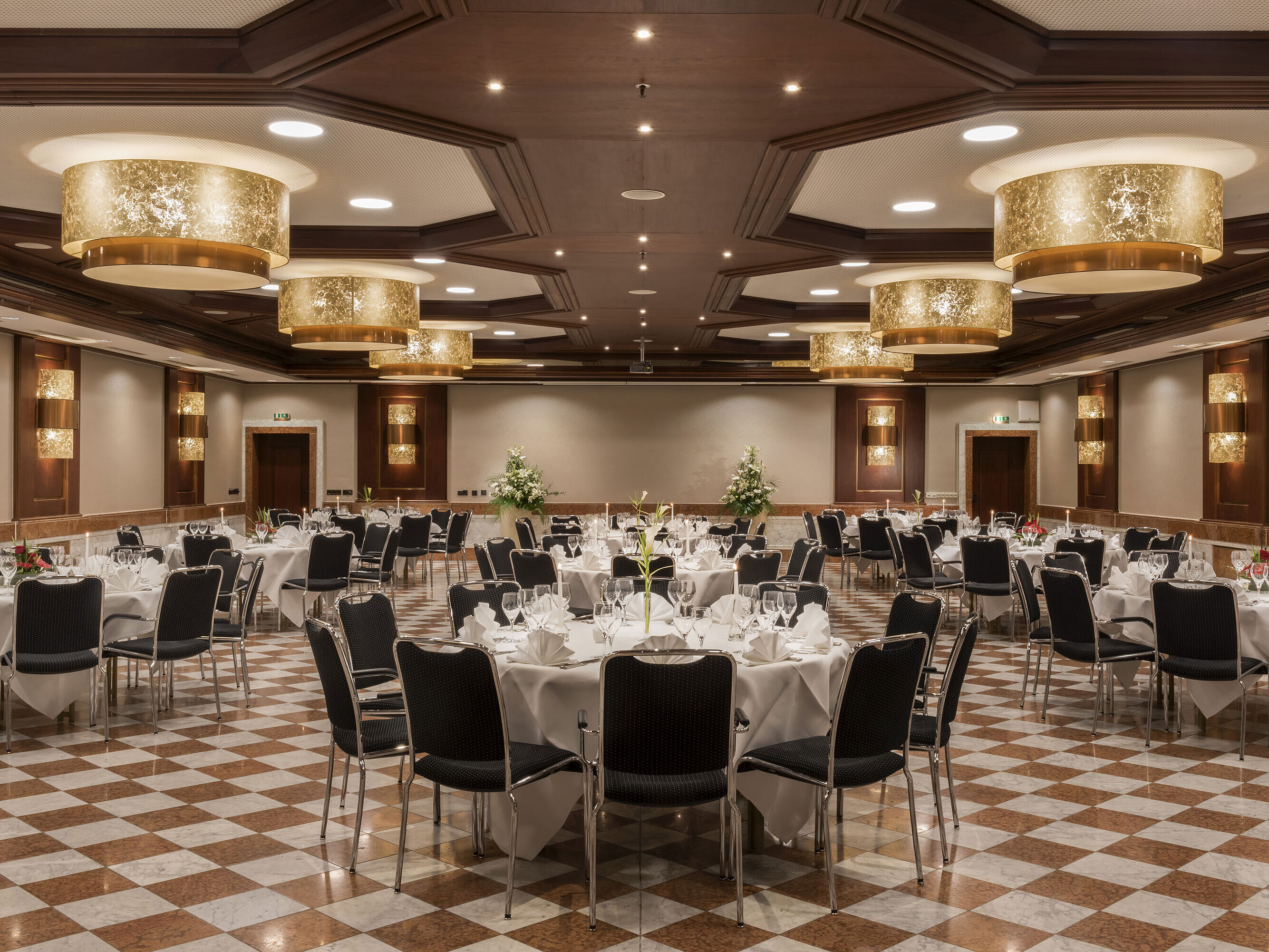 Elegante salón de eventos en Maritim Hotel Königswinter con mesas redondas, decoración elegante y lámparas.