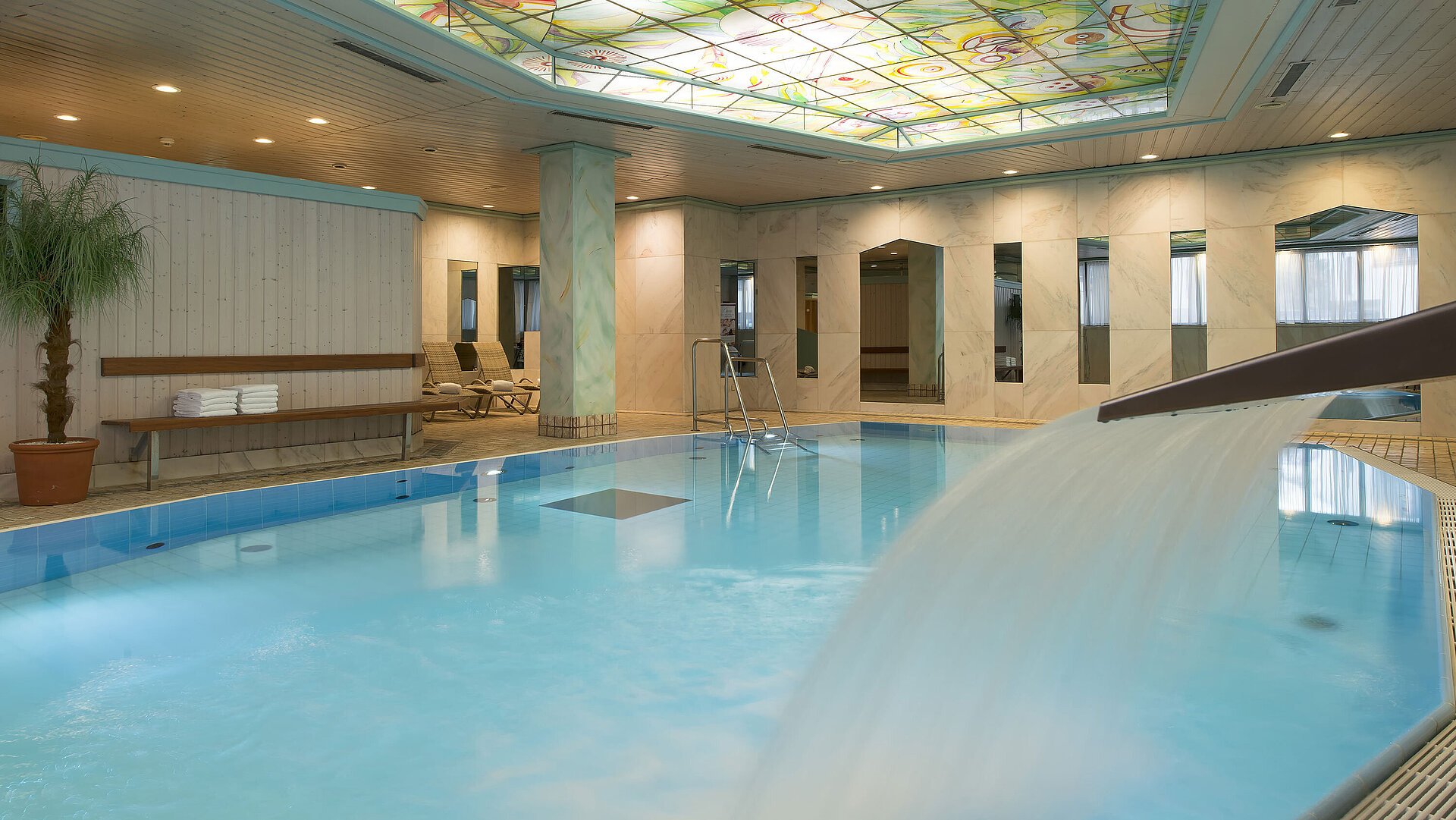 Piscina climatizada con cascada y techo de vidrio colorido