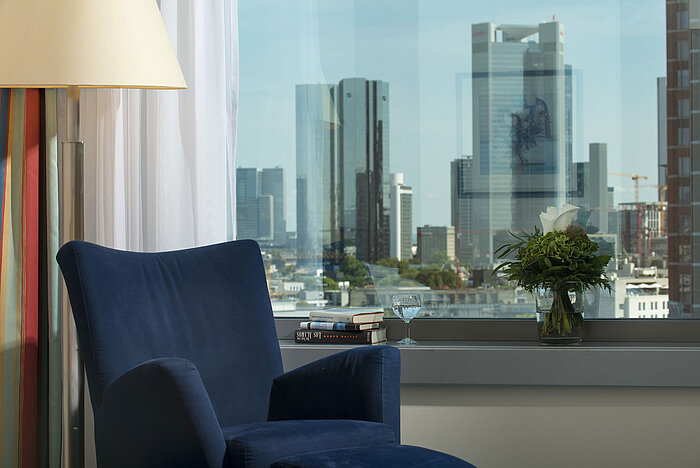 Vista da una suite al Maritim Hotel Frankfurt con skyline, poltrona blu e composizione floreale decorativa.