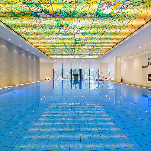 Élégant espace piscine au Maritim Bremen avec plafond en verre coloré et éclairage moderne, idéal pour bien-être et détente.