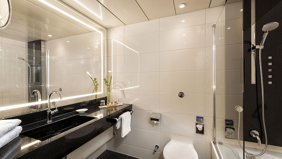 Salle de bains moderne avec douche et baignoire à l'Hôtel Maritim Bonn, équipée de luminaires élégants et miroir éclairé.