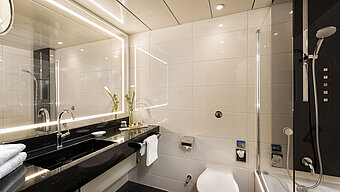 Baño moderno con ducha y bañera en el Hotel Maritim Bonn, con elegantes accesorios y espejo iluminado.