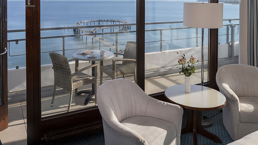 Camera d’hotel con area salotto e balcone con vista mare al Maritim Seehotel Timmendorfer Strand.