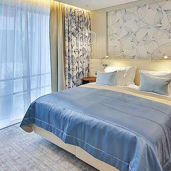 Habitación moderna con cama doble, detalles en azul y grandes ventanas con cortinas